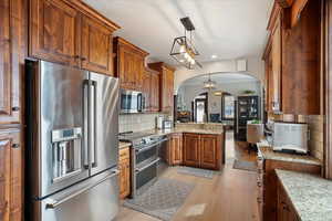 Kitchen featuring arched walkways, light stone counters, stainless steel appliances, tasteful backsplash, and pendant lighting