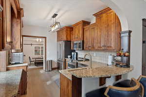 Kitchen featuring decorative light fixtures, backsplash, brown cabinetry, high quality appliances, and light wood-type flooring