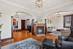 Living area with a fireplace with raised hearth, crown molding, baseboards, and wood finished floors