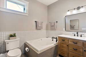 Bathroom with wainscoting, a garden tub, vanity, and toilet