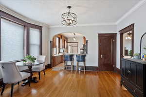 Dining area featuring a textured ceiling, light wood-style flooring, baseboards, ornamental molding, and an inviting chandelier