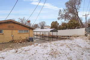 Yard layered in snow with central air condition unit and fence