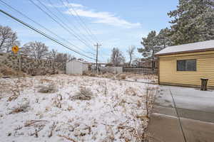 Snowy yard featuring fence, an outdoor structure, and a shed