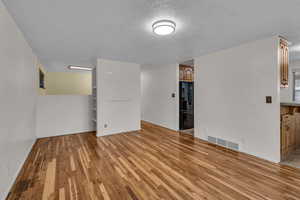 Living room featuring a textured ceiling, light wood-style flooring, visible vents, and baseboards