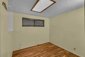 Spare room featuring a textured ceiling, light wood finished floors, a skylight, and baseboards