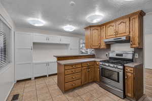 Kitchen featuring under cabinet range hood, brown cabinets, stainless steel range with gas stovetop, and light countertops