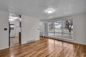 Living room featuring light wood-type flooring, visible vents, a textured ceiling, and baseboards