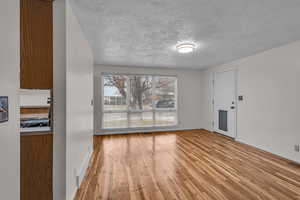 Living/dining area with light wood-style floors, visible vents, a textured ceiling, and baseboards