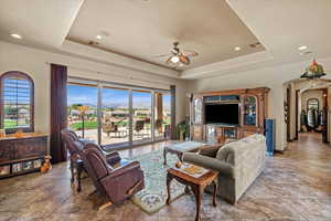 Living room with arched walkways, ceiling fan, a tray ceiling, and visible vents