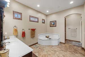 Bathroom with recessed lighting, a garden tub, vanity, and baseboards