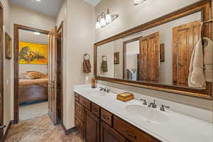 Ensuite bathroom featuring double vanity, baseboards, a sink, and ensuite bathroom