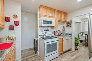 Kitchen featuring light countertops, light wood-style flooring, light brown cabinets, white appliances, and baseboards