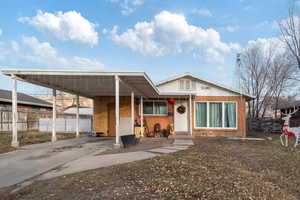 View of front of property with an attached carport, concrete driveway, brick siding, and fence