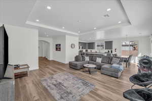 Living area featuring arched walkways, visible vents, baseboards, light wood finished floors, and a tray ceiling