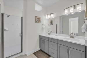 Bathroom with double vanity, a stall shower, a sink, and baseboards