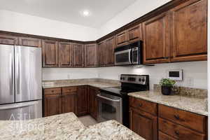 Kitchen with stainless steel appliances, light tile patterned flooring, light stone counters, dark brown cabinets, and recessed lighting
