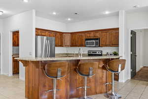 Kitchen with light tile patterned floors, a kitchen bar, light stone countertops, appliances with stainless steel finishes, and an island with sink
