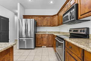 Kitchen featuring appliances with stainless steel finishes, light stone counters, brown cabinets, light tile patterned floors, and recessed lighting