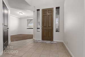 Foyer with light tile patterned flooring, light colored carpet, and baseboards