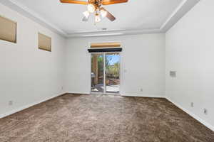 Unfurnished room featuring a tray ceiling, dark colored carpet, and a ceiling fan