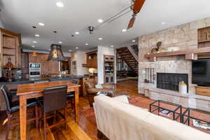 Living room with hardwood / wood-style floors, a stone fireplace, sink, and ceiling fan