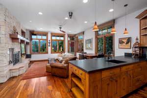 Kitchen featuring pendant lighting, sink, a kitchen island with sink, a fireplace, and dark hardwood / wood-style flooring