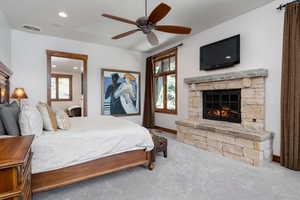 Carpeted bedroom with a stone fireplace and ceiling fan