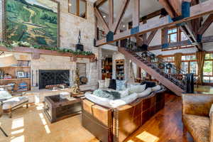 Living room featuring hardwood / wood-style floors, beam ceiling, high vaulted ceiling, and a stone fireplace