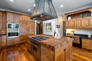 Kitchen with stainless steel stove, wooden counters, island range hood, built in desk, and a kitchen island