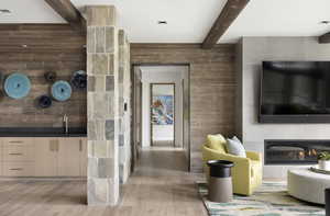 Interior space with a glass covered fireplace, beamed ceiling, wood finished floors, and wood walls