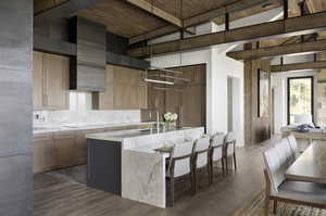 Kitchen featuring dark wood-style floors, black electric stovetop, hanging light fixtures, a sink, and an island with sink