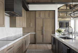 Kitchen featuring light wood finished floors, light stone counters, black electric cooktop, premium range hood, and a sink