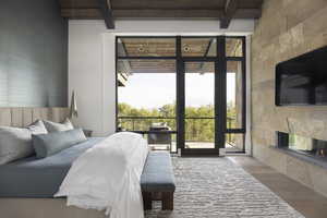 Bedroom with multiple windows, beamed ceiling, a fireplace, and wood finished floors