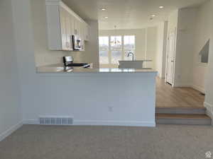 Kitchen featuring stainless steel appliances, a peninsula, visible vents, white cabinets, and light countertops