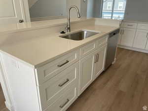 Kitchen with a sink, white cabinetry, light countertops, and stainless steel dishwasher