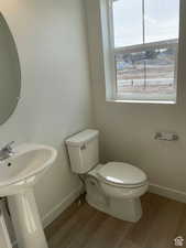 Half bathroom with baseboards, toilet, and wood finished floors