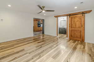 Unfurnished room with light wood finished floors, a barn door, and baseboards