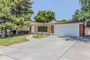 Tri-level home featuring an attached garage, brick siding, concrete driveway, stone siding, and a front yard