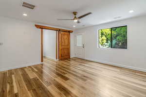 Unfurnished room with light wood-style floors, visible vents, and a barn door