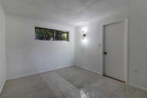 Spare room featuring a textured ceiling, light carpet, and baseboards