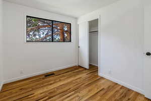 Unfurnished bedroom featuring a closet, visible vents, baseboards, and wood finished floors