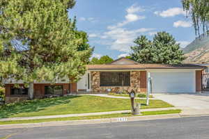 View of front facade with driveway, a garage, stone siding, a mountain view, and a front lawn