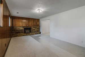 Unfurnished living room with visible vents, light colored carpet, a stone fireplace, wooden walls, and a textured ceiling