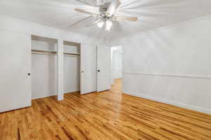 Unfurnished bedroom with ceiling fan, ornamental molding, two closets, and light wood-style floors