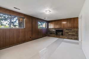 Unfurnished living room featuring wood walls, a fireplace, and visible vents