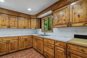 Kitchen featuring brick floor, brown cabinetry, light countertops, and a sink
