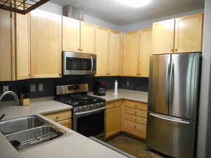 Kitchen with light brown cabinets, light countertops, appliances with stainless steel finishes, and a sink