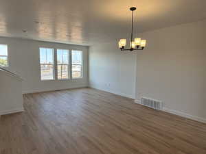 Empty room with an inviting chandelier, baseboards, visible vents, and wood finished floors