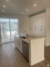 Kitchen featuring a kitchen island with sink, a sink, white cabinetry, light countertops, and dishwasher