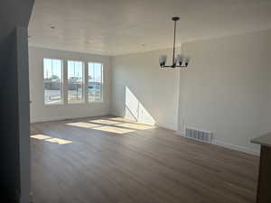 Unfurnished room with visible vents, a textured ceiling, wood finished floors, a chandelier, and baseboards